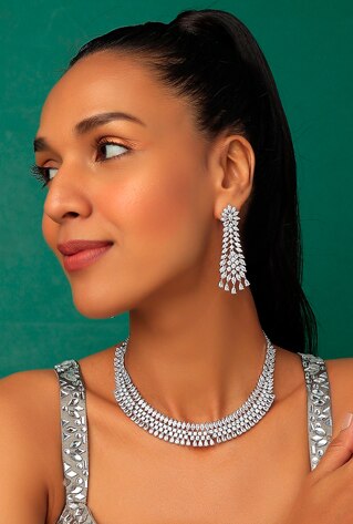 A white finish necklace studded with faux diamonds, set in mixed metal. It is paired with a matching pair of earrings.
