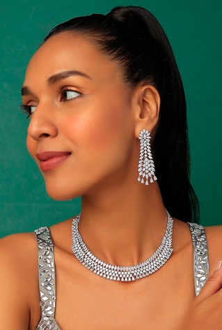 A white finish necklace studded with faux diamonds, set in mixed metal. It is paired with a matching pair of earrings.