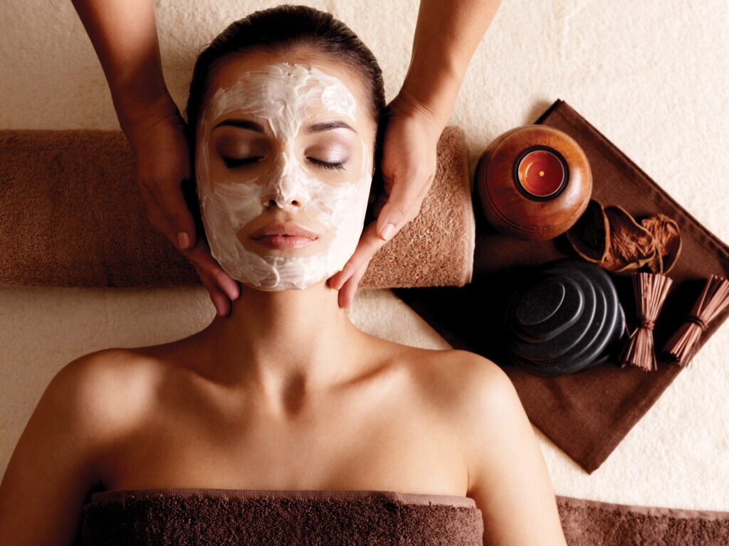 Spa massage for young woman with facial mask on face - indoors