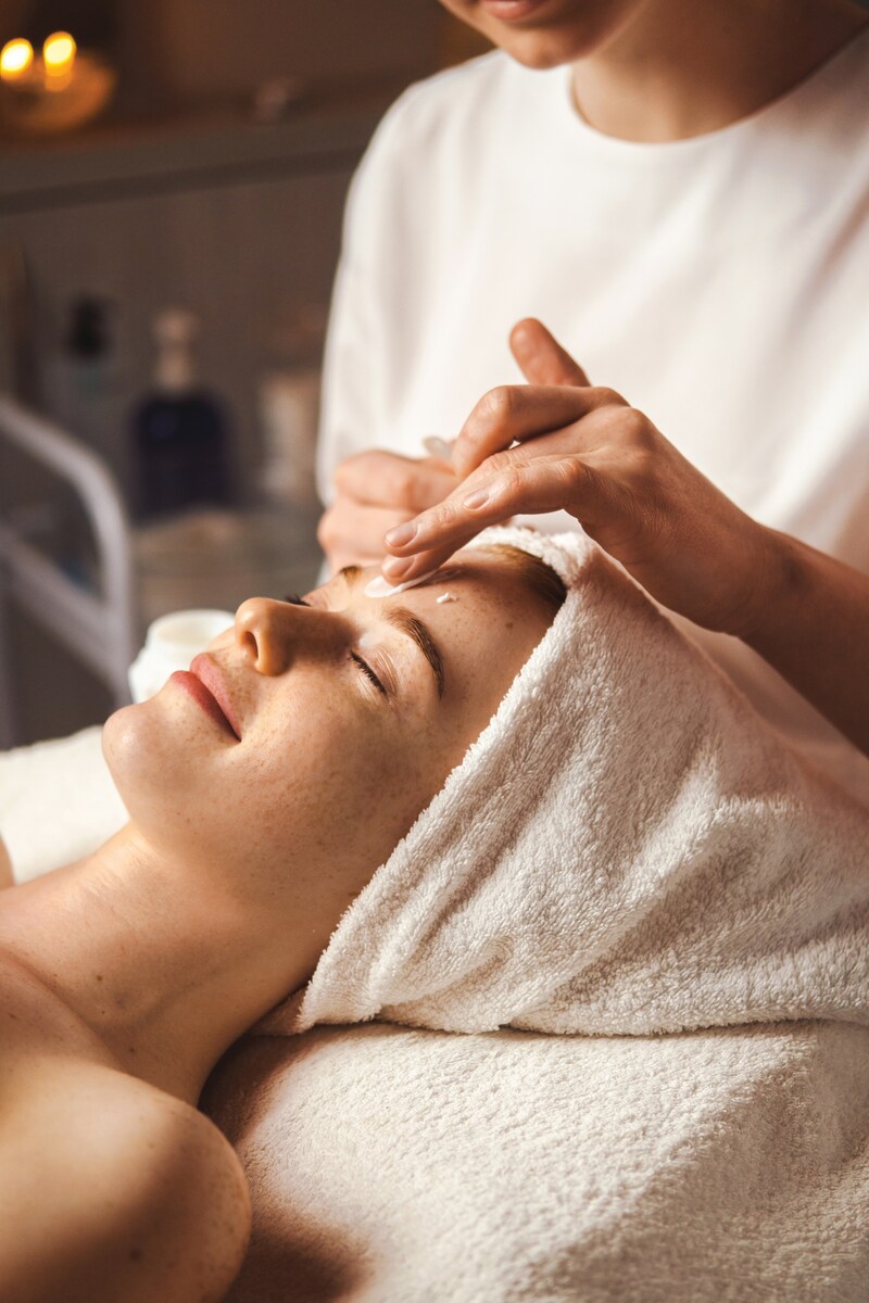 Beautician applying facial cream all over young woman's forehead at spa salon. Skin treatment. Girl facial treatment. Medical health.