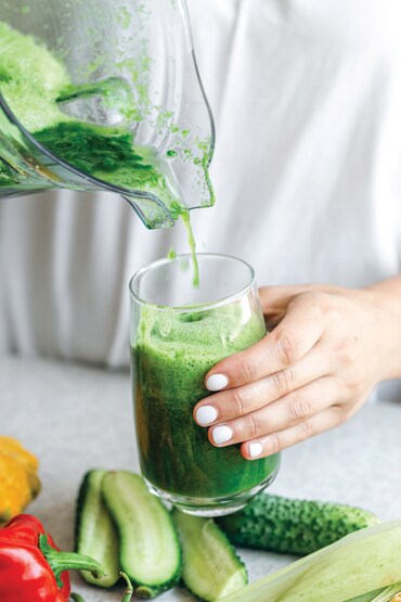 A woman pouring green smoothie to glass, healthy food concept.