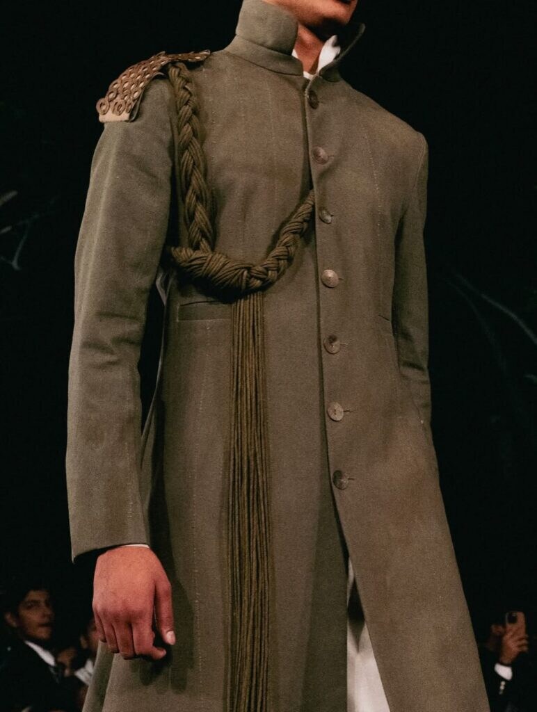 Model wearing a candy-striped bandhgala jacket paired with oversized bermuda pants and a leheriya headpiece.