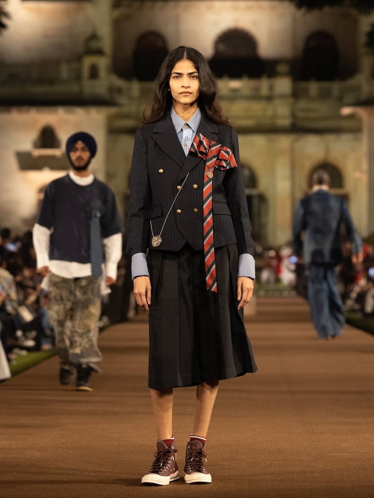 Model wearing a candy-striped bandhgala jacket paired with oversized bermuda pants and a leheriya headpiece